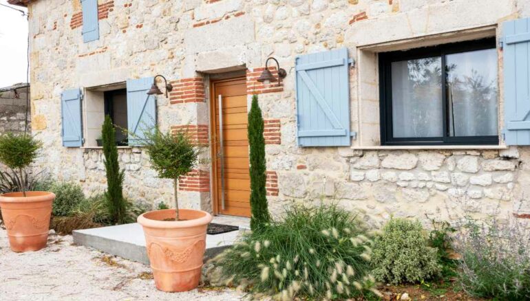 une porte entrée en bois Nativ 3 sur une grande maison en pierre avec des volets bleus