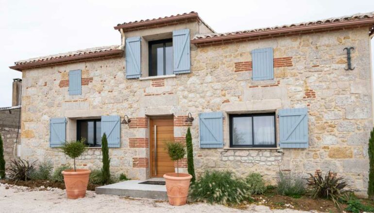 une porte entrée en bois Nativ 3 sur une grande maison en pierre avec des volets bleus